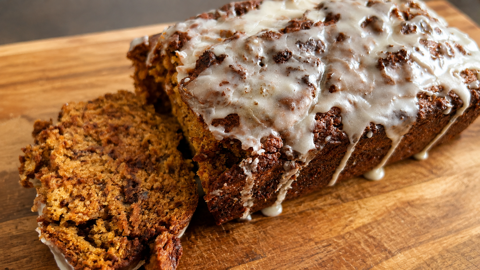 Sliced cinnamon swirl banana bread topped with vanilla icing on a wooden cutting board.